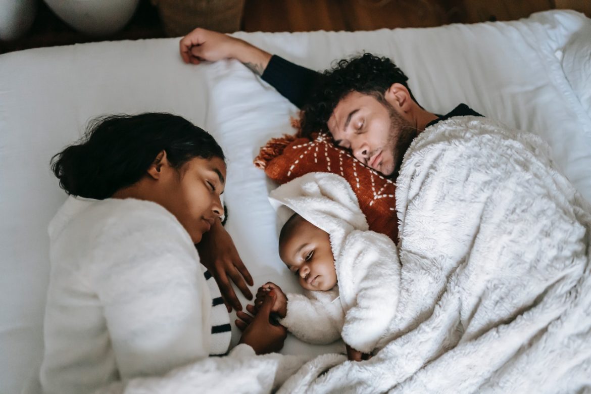 Beitragsbild zu "Wann haben Eltern eigentlich Sex?": Eine schwarze Frau, ein schwarzes Baby und ein weißer Mann liegen schlafend in einem Bett